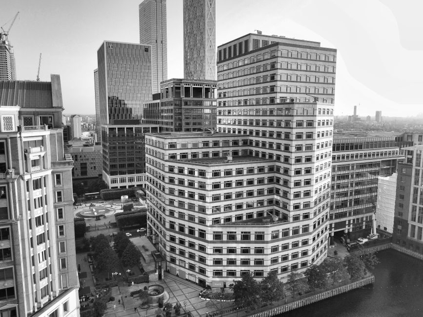 A panoramic view of Canary Wharf in London showcasing a cluster of modern high-rise buildings along the river Thames under clear blue skies during daytime. Prominent structures include the HSBC and Ci